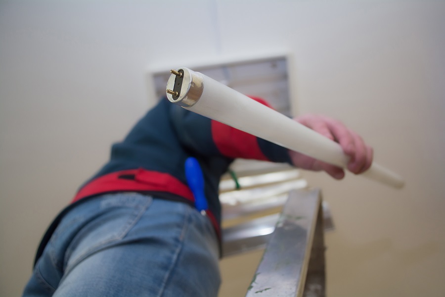 Electrician man worker in uniform installing ceiling fluorescent lamp